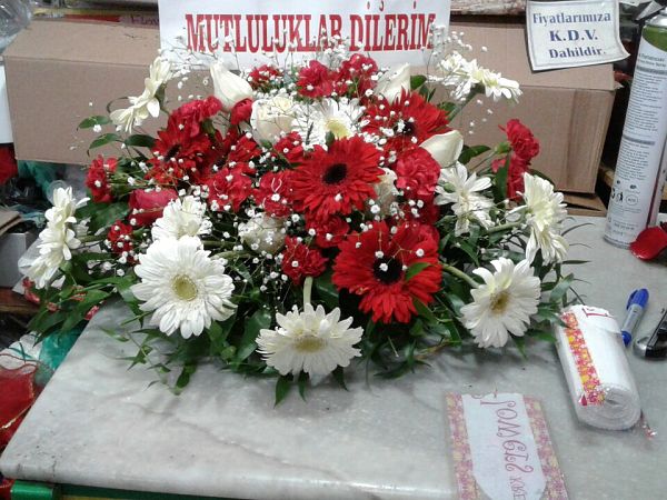 Üzerinde “Mutluluklar dileriz” yazılı kart bulunan, kırmızı gül ve beyaz gerberalı masa aranjmanı